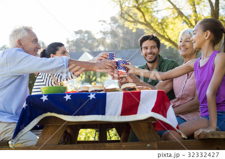 Happy family toasting the cups while having meal in the park Happy family toasting the cups while having meal in the park 32332427