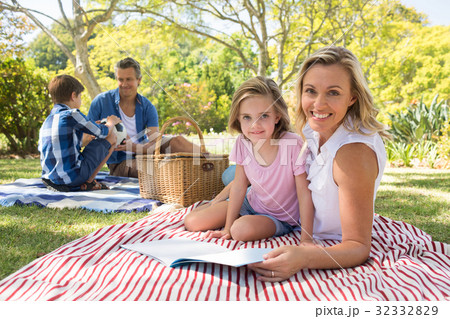 Mother and daughter reading book while father and son playing with football in park Mother and daughter reading book while father and son playing with football in park 32332829