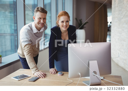 Portrait of smiling executives standing at desk Portrait of smiling executives standing at desk 32332880