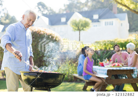 Senior man preparing barbecue while family having meal Senior man preparing barbecue while family having meal 32332882