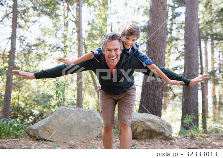 Cheerful father piggybacking son while hiking in forest 32333013