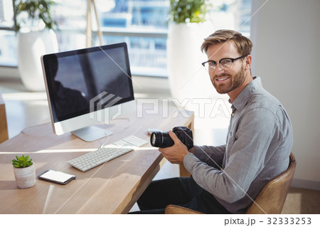 Portrait of smiling executive holding digital camera at desk Portrait of smiling executive holding digital camera at desk 32333253