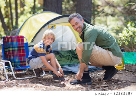 Smiling father and son tying shoelace by tent at campsite Smiling father and son tying shoelace by tent at campsite 32333297