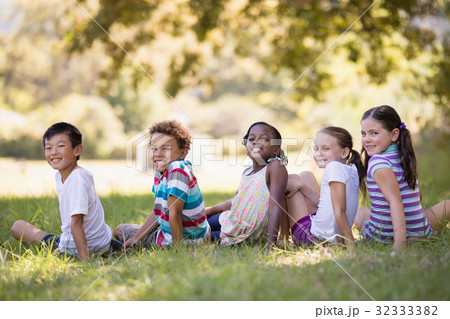Smiling friends sitting on grass at campsit Smiling friends sitting on grass at campsit 32333382