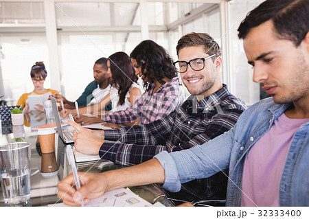 Smiling businessman sitting amidst colleagues working at office 32333400