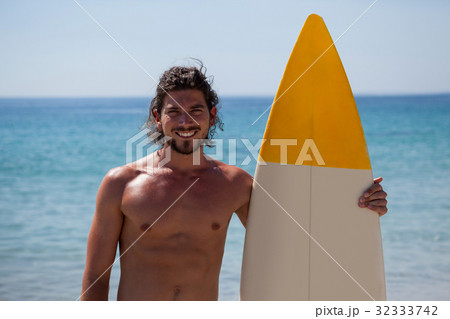 Smiling surfer with surfboard standing at beach coast Smiling surfer with surfboard standing at beach coast 32333742
