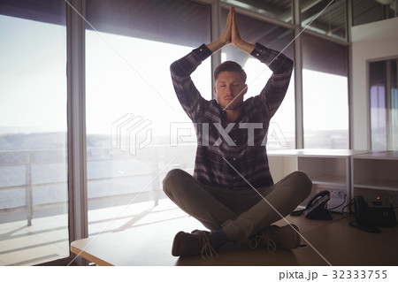 Young businessman meditating on table at office 32333755