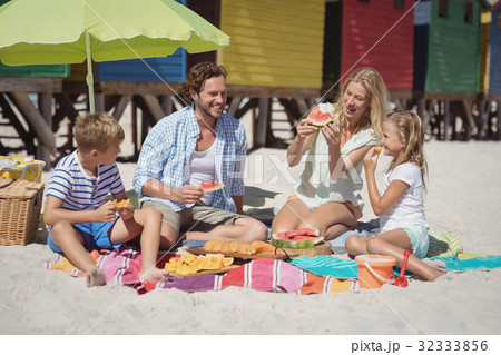 Happy family eating watermelon while sitting together at beach 32333856
