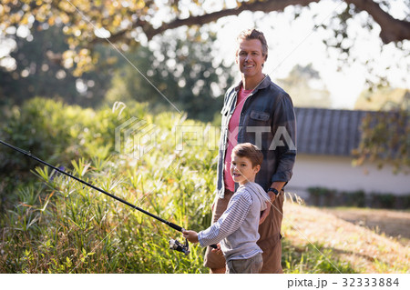 Portrait of father standing by boy holding fishing rod Portrait of father standing by boy holding fishing rod 32333884