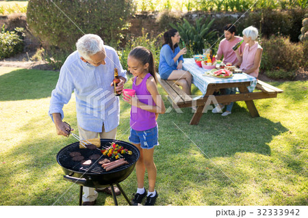Grandfather and granddaughter preparing barbecue while family having meal Grandfather and granddaughter preparing barbecue while family having meal 32333942