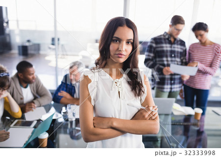 Portrait of young businesswoman standing with team working in background 32333998