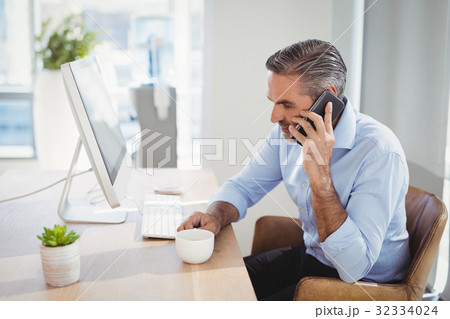 Executive talking on mobile phone at desk Executive talking on mobile phone at desk 32334024