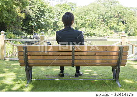公園のベンチで通話をするビジネスマン後ろ姿 の写真素材