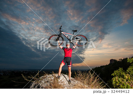 Cyclist raising the mountain bike above his head with success Cyclist raising the mountain bike above his head with success 32449412