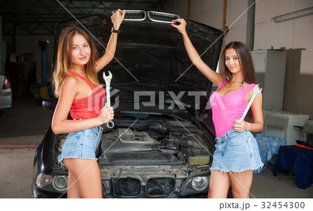 Two girls standing by the car at auto repair shop Two girls standing by the car at auto repair shop 32454300
