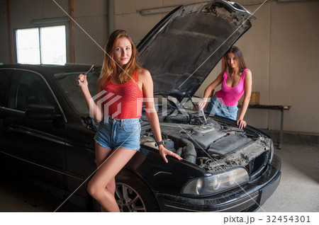 Two girls standing by the car at auto repair shop Two girls standing by the car at auto repair shop 32454301