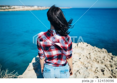 Back view of young woman with wind in her hair standing on cliff 32459096