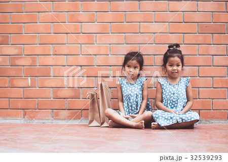 Two girls sitting and hugging their knees Two girls sitting and hugging their knees 32539293