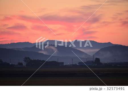 夜明け前の青い山影と民家と朱色の朝焼けの風景を撮影 32573491