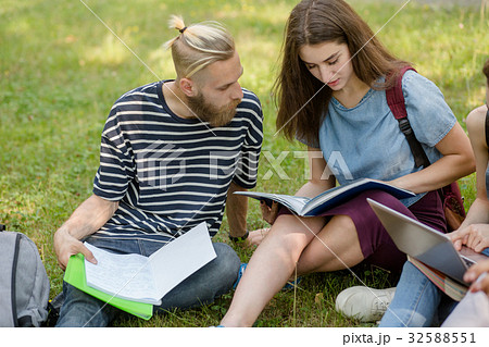 Students boy and girl sitting on grass studying. 32588551