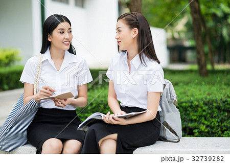Two female students are sitting and discussing lesson outdoors 32739282