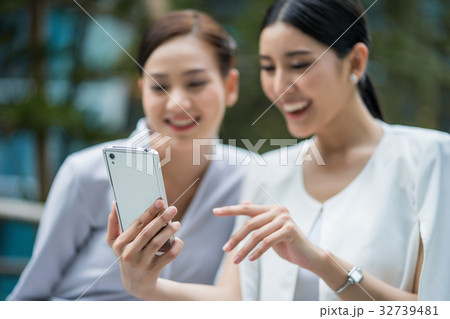 two women are looking, using their phone and smiling happily. 32739481