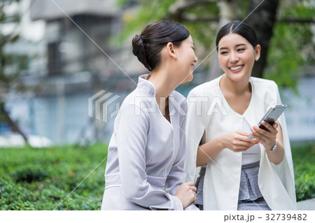 a picture of two women using their phone and smiling happily outdoors a picture of two women using their phone and smiling happily outdoors 32739482
