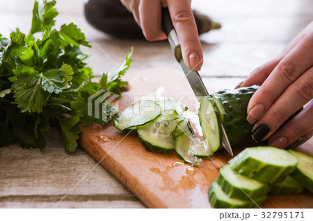Woman cuts cucumber on wooden desk Woman cuts cucumber on wooden desk 32795171