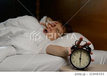 Young woman turning off the alarm clock on the bed Young woman turning off the alarm clock on the bed 32846503