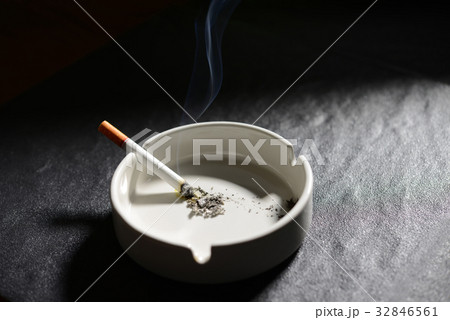 Lit cigarette lying on an empty white ashtray 32846561