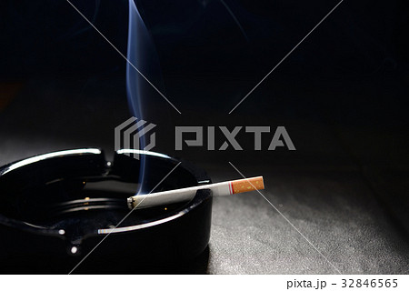 Lit cigarette with smoke lying on an empty ashtray 32846565