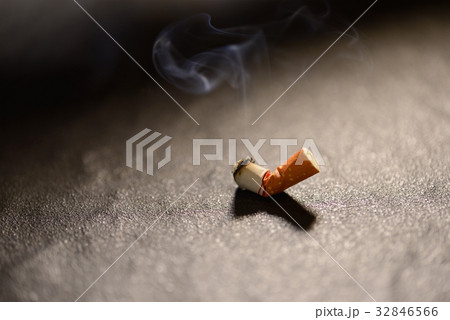 Lit cigarette butt with smoke on the ground 32846566