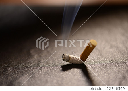 Lit cigarette butt with smoke on the ground 32846569