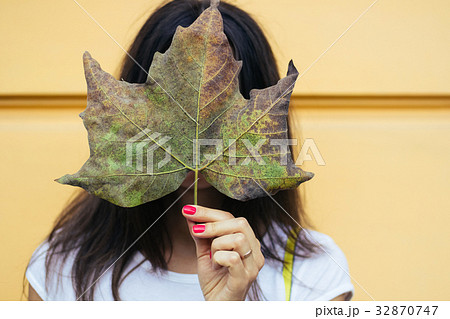 Young woman holding a fallen leaf in the face 32870747