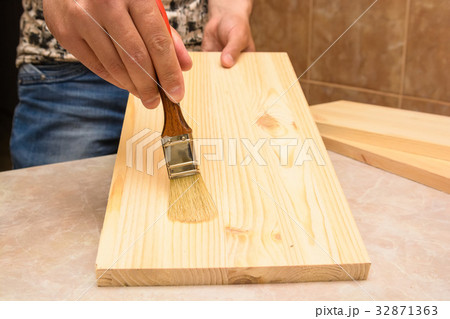 Hand holding brush polishes wooden plank 32871363