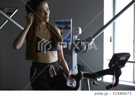 A woman is listening with earphone and holding a bottle of water at fitness center A woman is listening with earphone and holding a bottle of water at fitness center 32886671