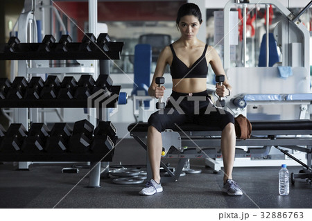 A Thai woman is lifting dumbbells and looking at camera. 32886763