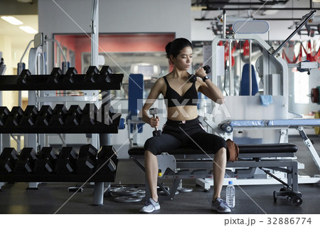A Thai woman is using two hands to lift dumbbells in a fitness club. 32886774