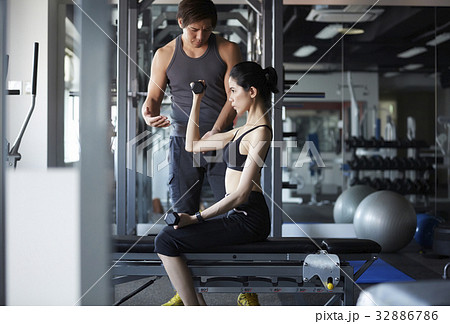 A Thai instructor is training weight lifting for a woman in a gym. 32886786