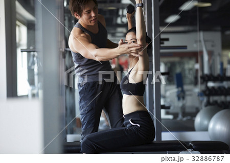 Thai woman is listening to the instructor 's instruction to adjust lifting weights posture. Thai woman is listening to the instructor 's instruction to adjust lifting weights posture. 32886787