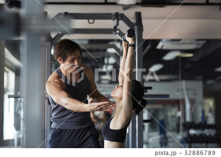 A photo of Thai instructor adjusting woman 's lifting weights posture in a gym. 32886789