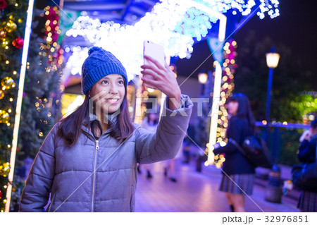 Woman taking selfie by mobile phone with christmas decoration at ngiht Woman taking selfie by mobile phone with christmas decoration at ngiht 32976851