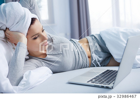 smiley young woman lying in her bed with laptop 32986467