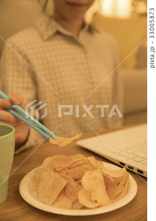 夜、パソコン作業をしながら箸(トング)でポテトチップスを食べる女性 夜、パソコン作業をしながら箸(トング)でポテトチップスを食べる女性 33005873