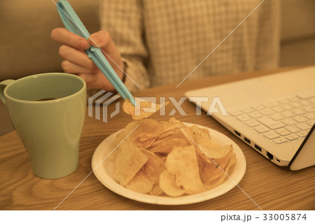 夜、パソコン作業をしながら箸(トング)でポテトチップスを食べる女性 33005874