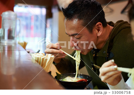 the man is eating noodles in the restaurant 33006758
