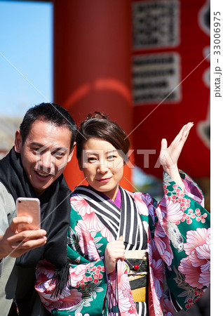 A beautiful couple is posing and smiling outside to selfie. 33006975