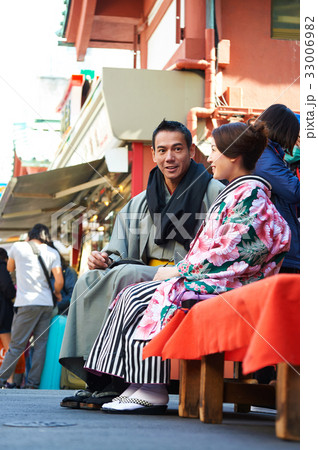 A young couple in kimono is sitting, chatting, smiling happily outside. 33006982