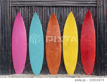 Colored surfboards leaning up against a wooden 33033073