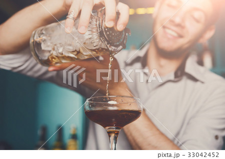 Young bartender pouring cocktail drink into glass 33042452